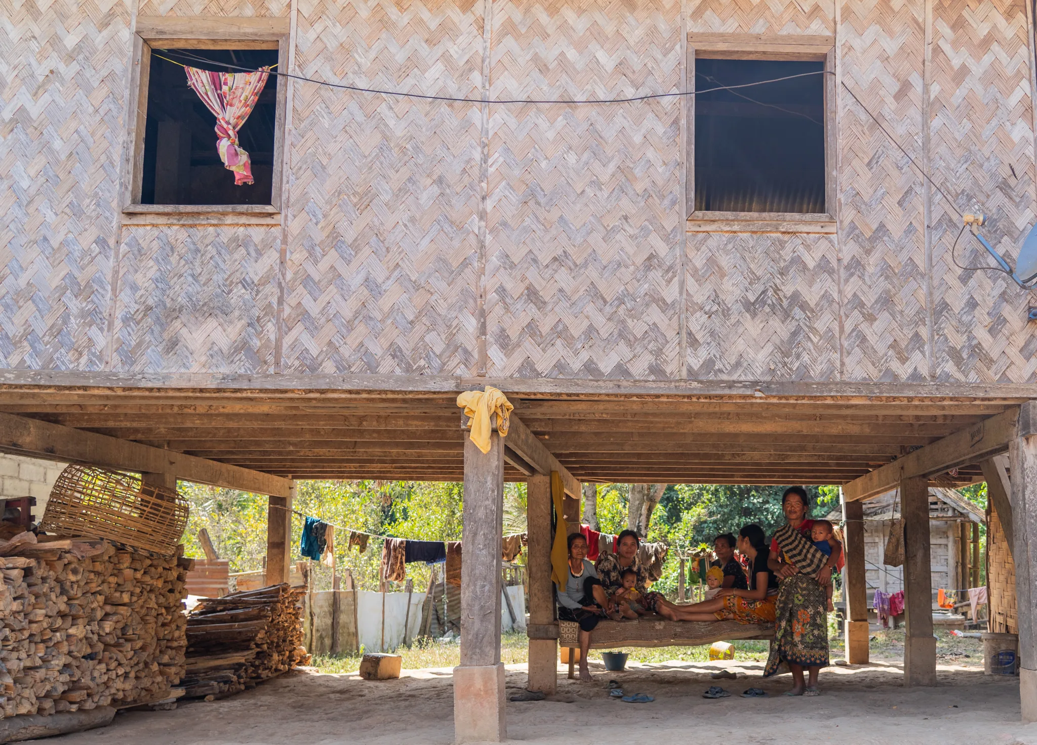 Extended family gathers beneath a stilted bamboo house, Laos