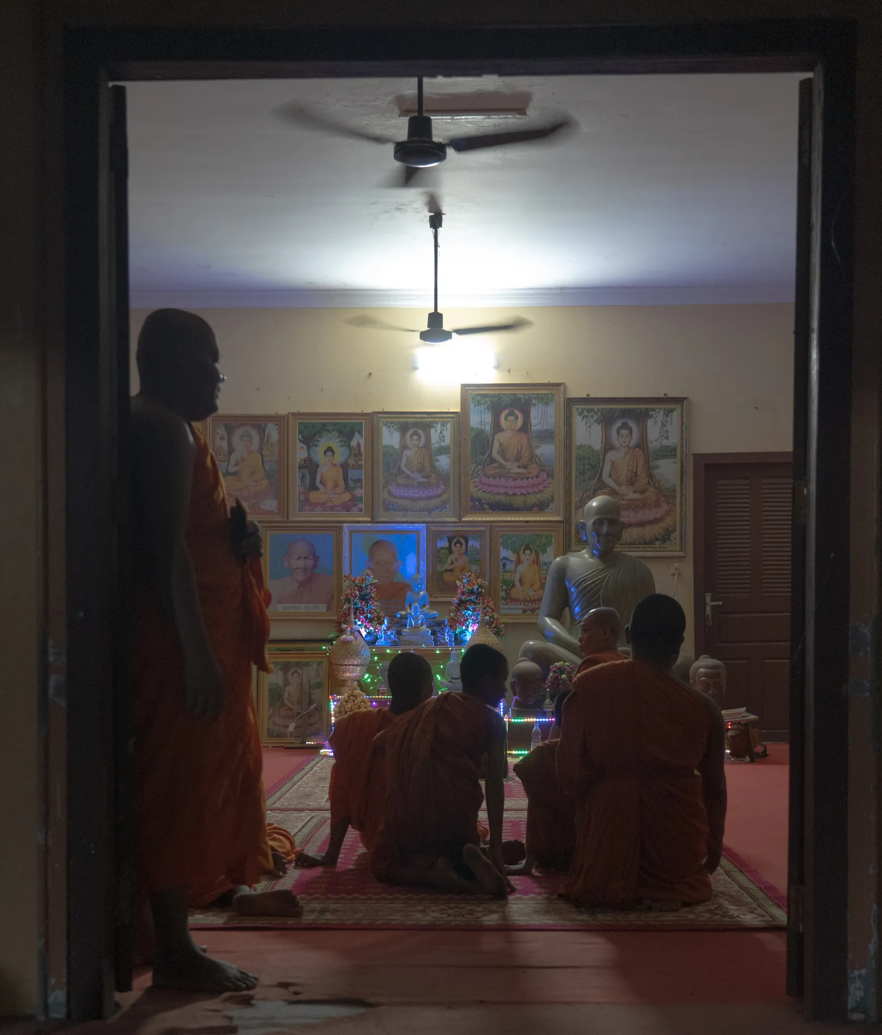 Monks kneeling before a wall of Buddha portraits, Cambodia