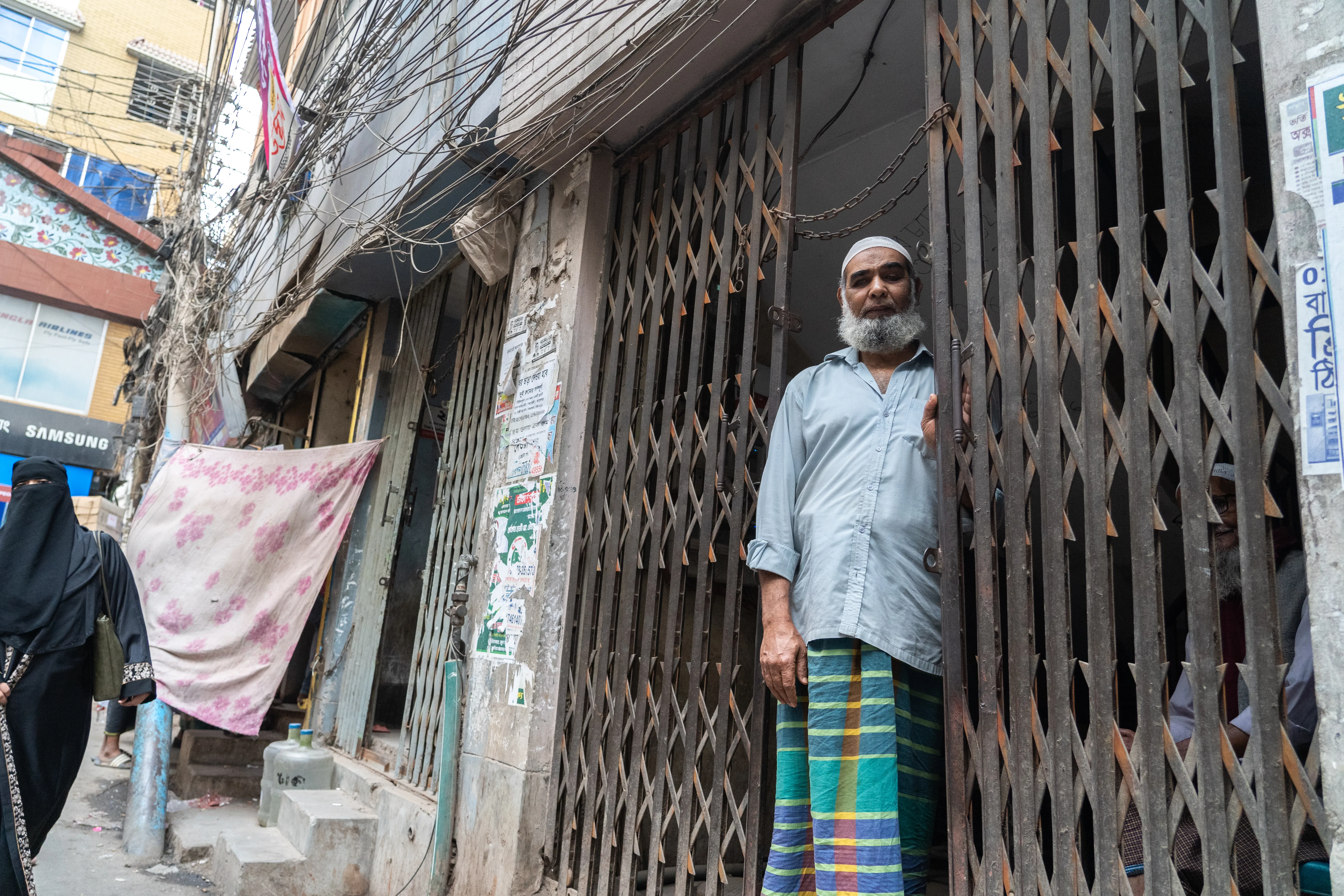 Shopkeeper standing in his gated doorway, Bangladesh