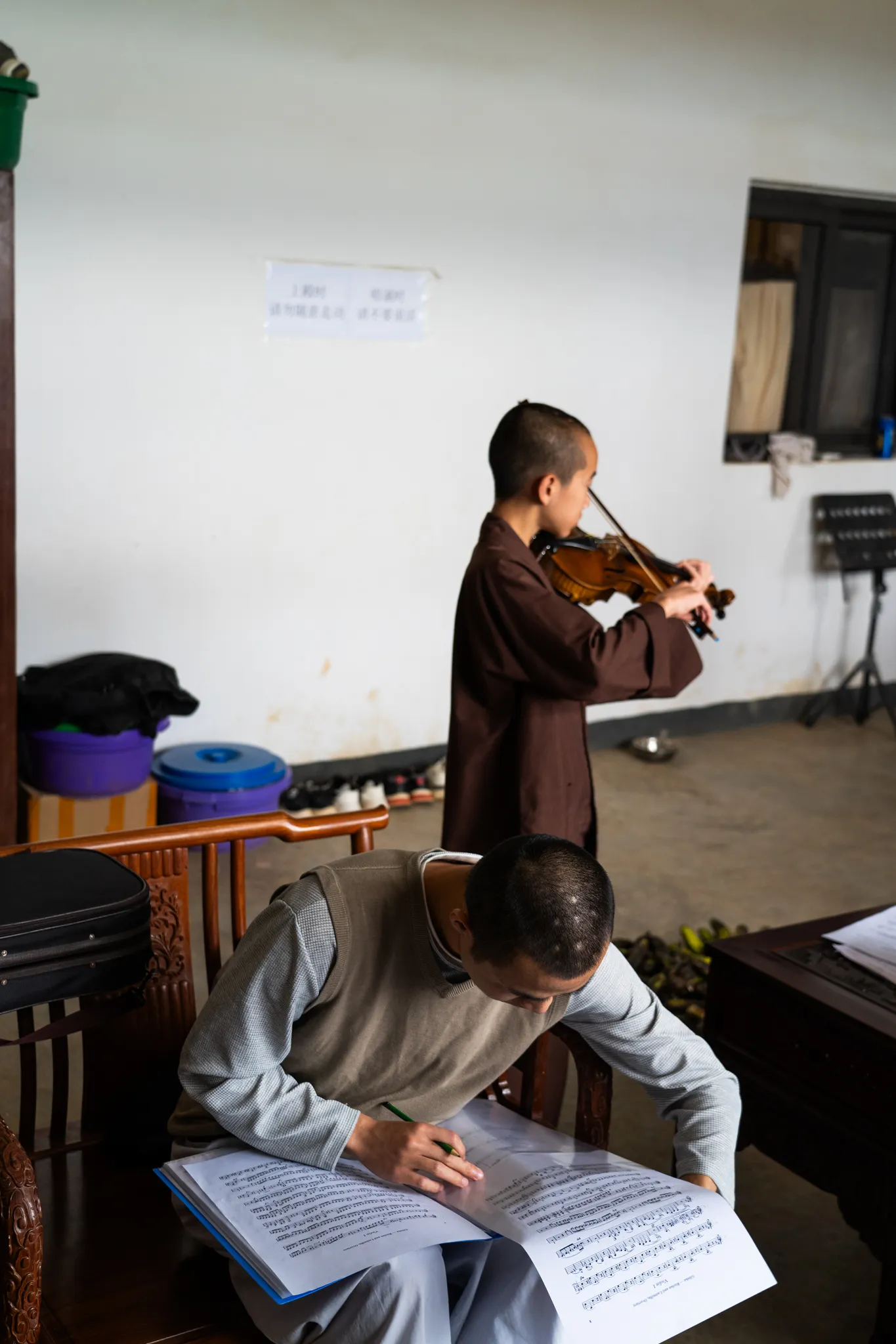 Monk practices violin while another marks up sheet music, Madagascar