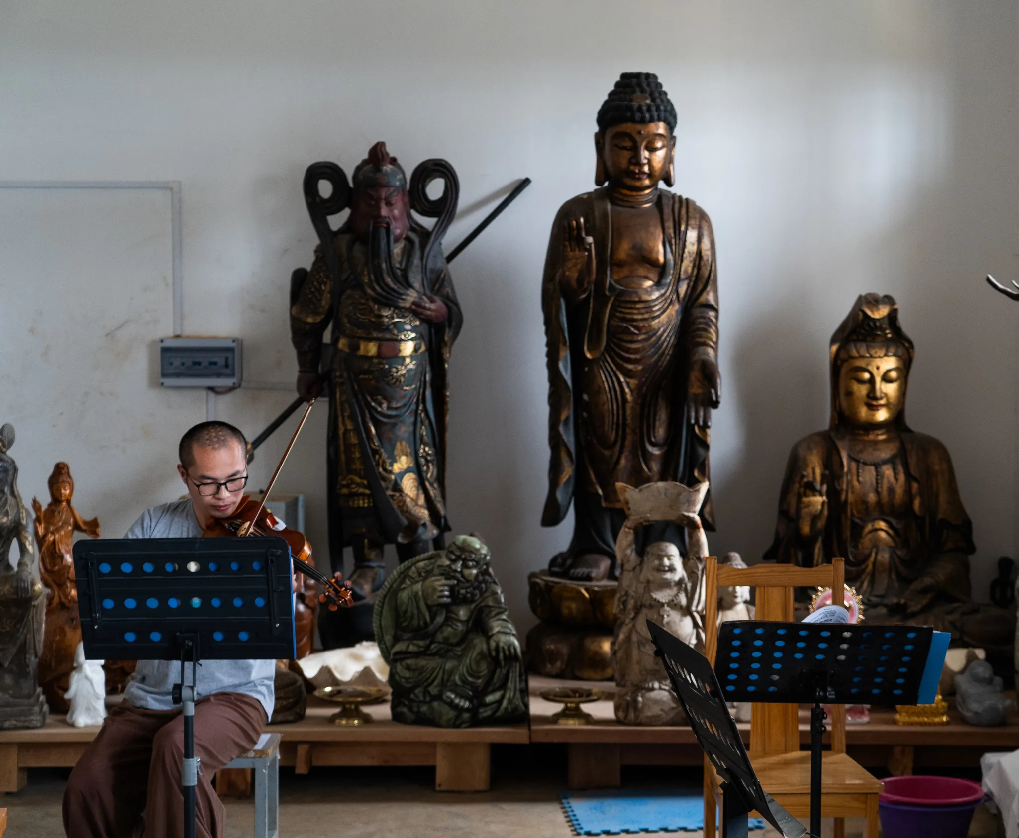 A young monk rehearses violin beside towering gilded statues, Madagascar