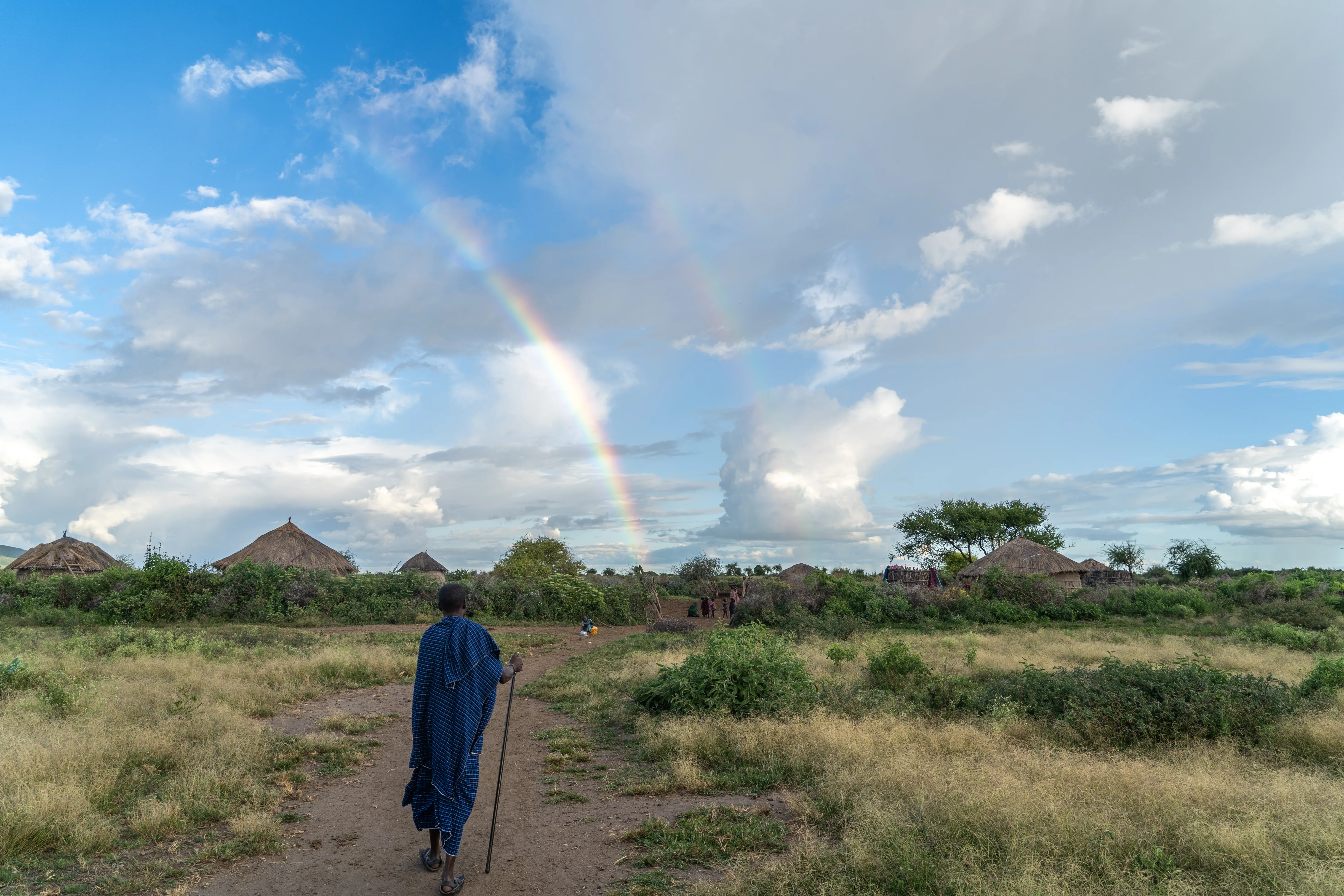 Massai man walking toward the village beneath a double rainbow, Tanzania