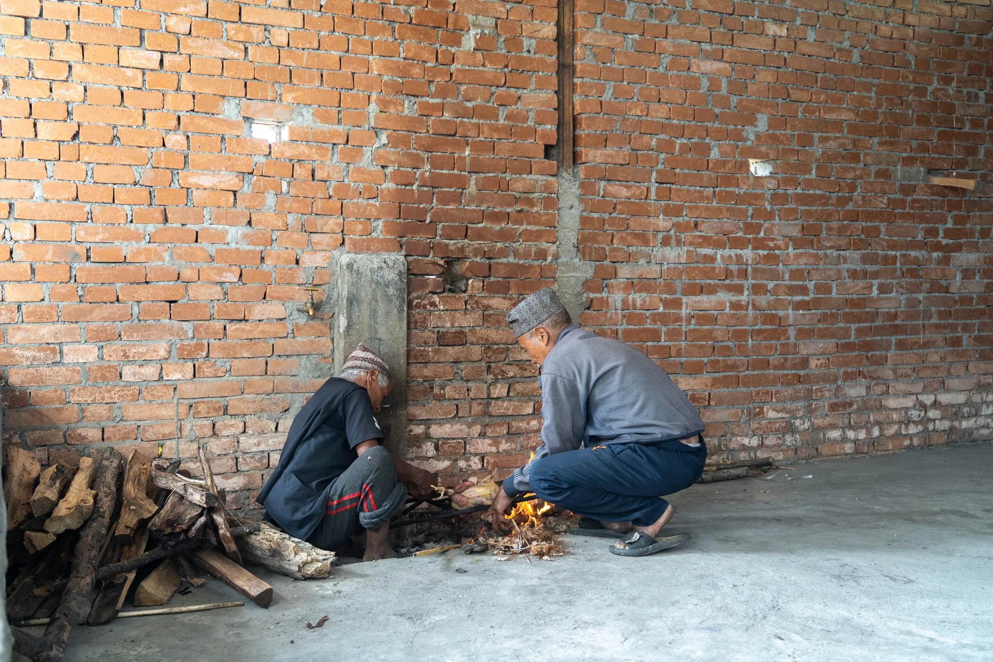 Two men tending a fire against a brick wall, Nepal