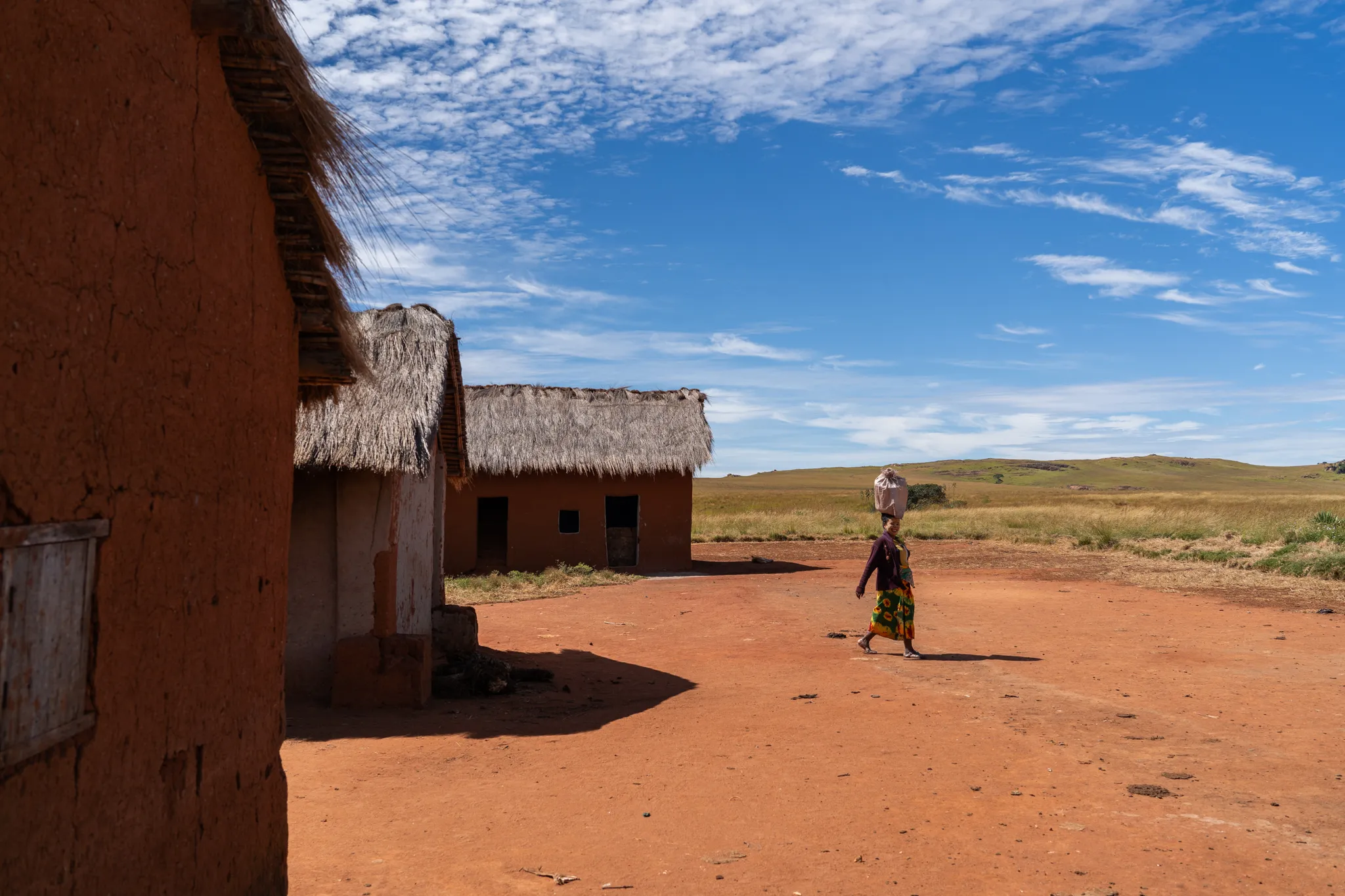Bara woman carrying a basket past homes, Madagascar