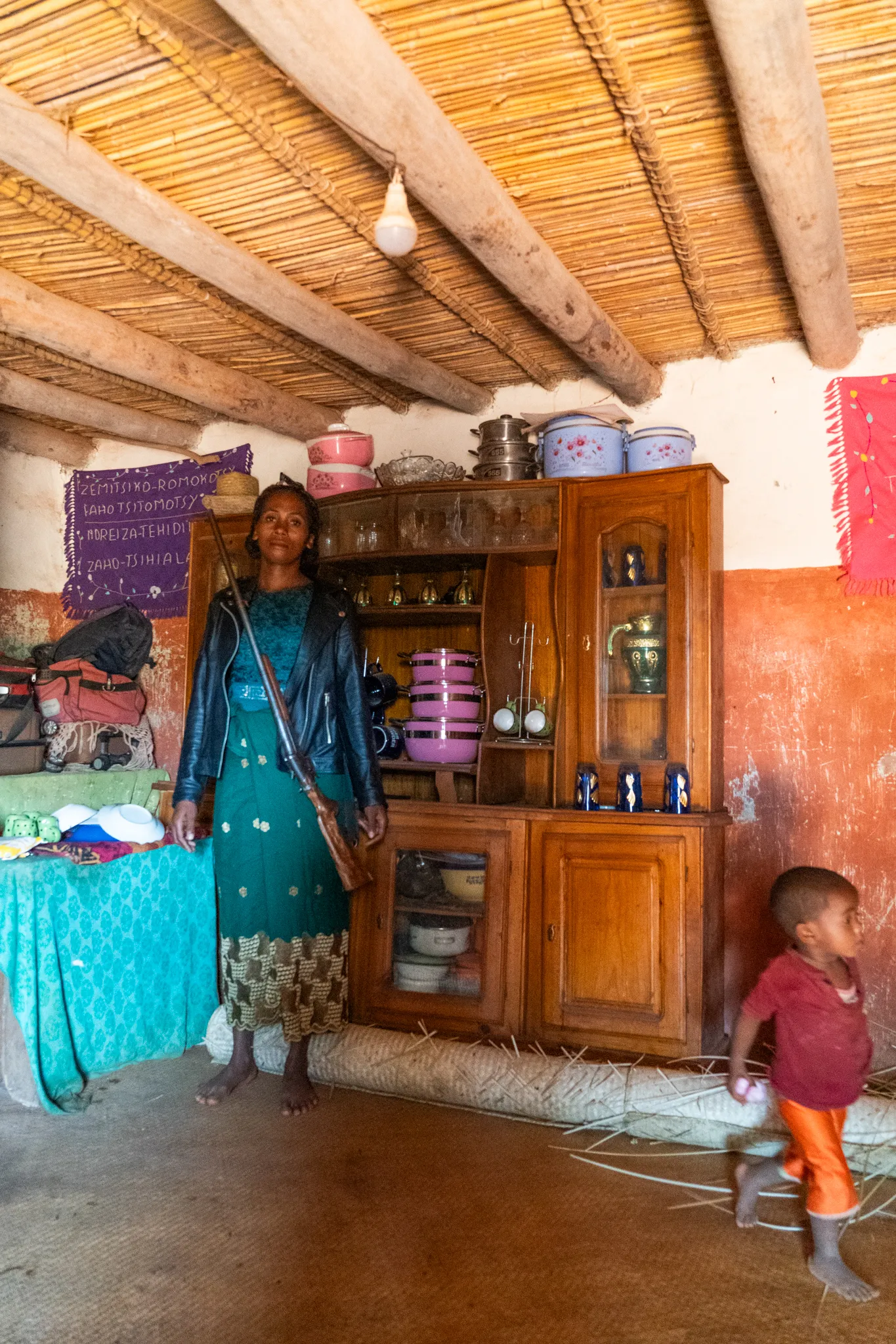 Bara woman with a rifle inside her home with her baby, Madagascar