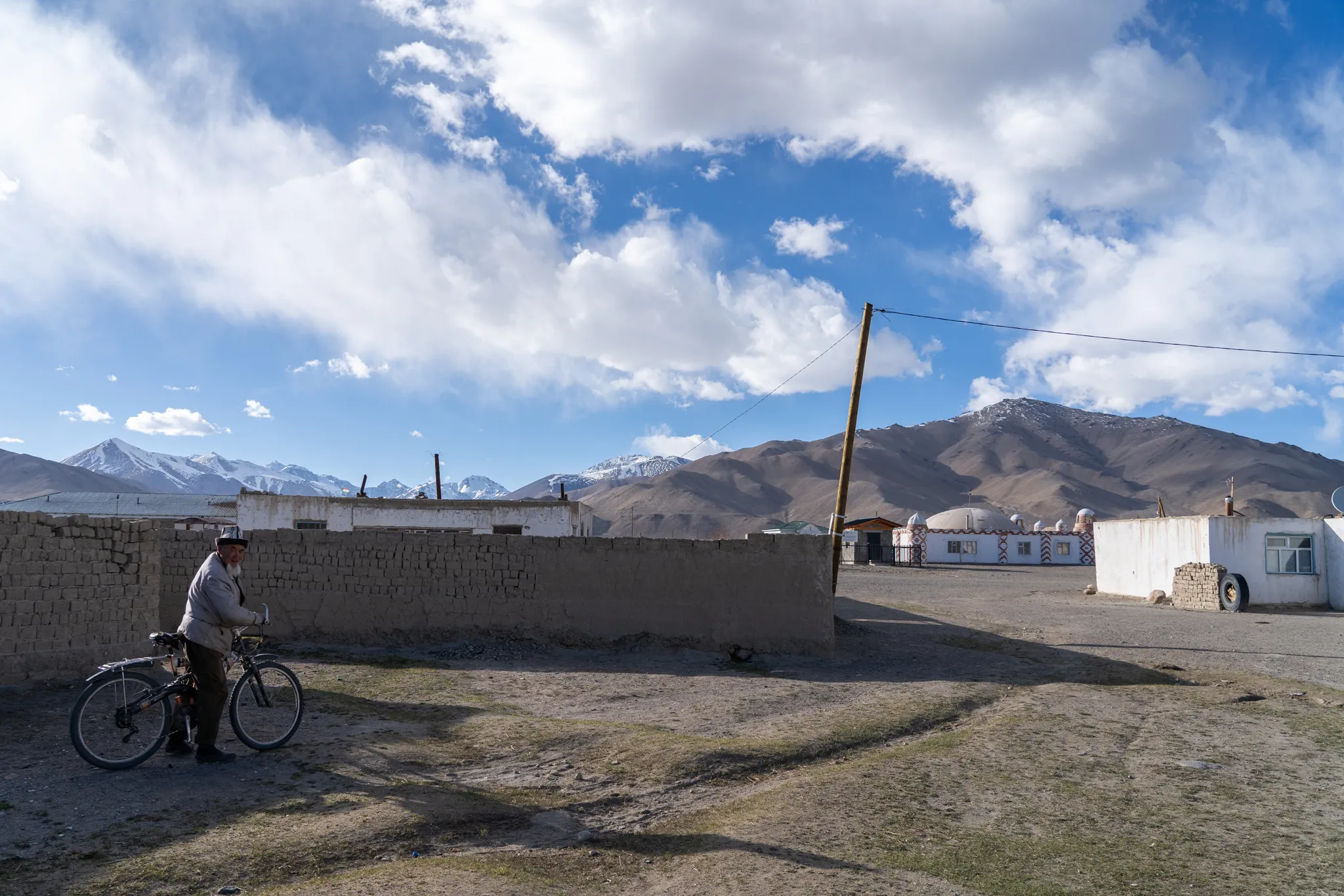 Elderly man with bicycle beside mud-brick wall, Tajikistan