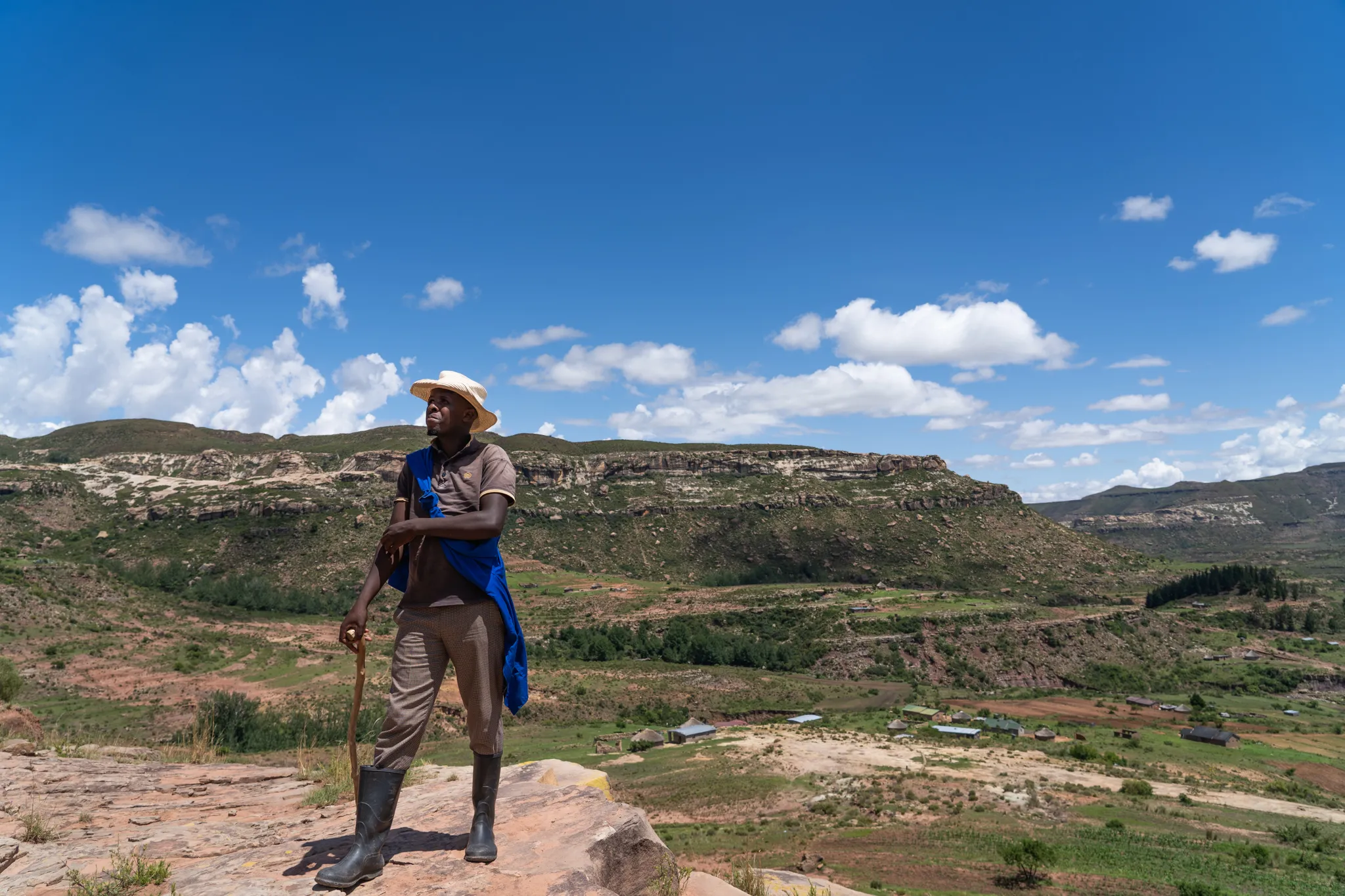 Herdboy pauses on a cliff above a wide valley, Lesotho