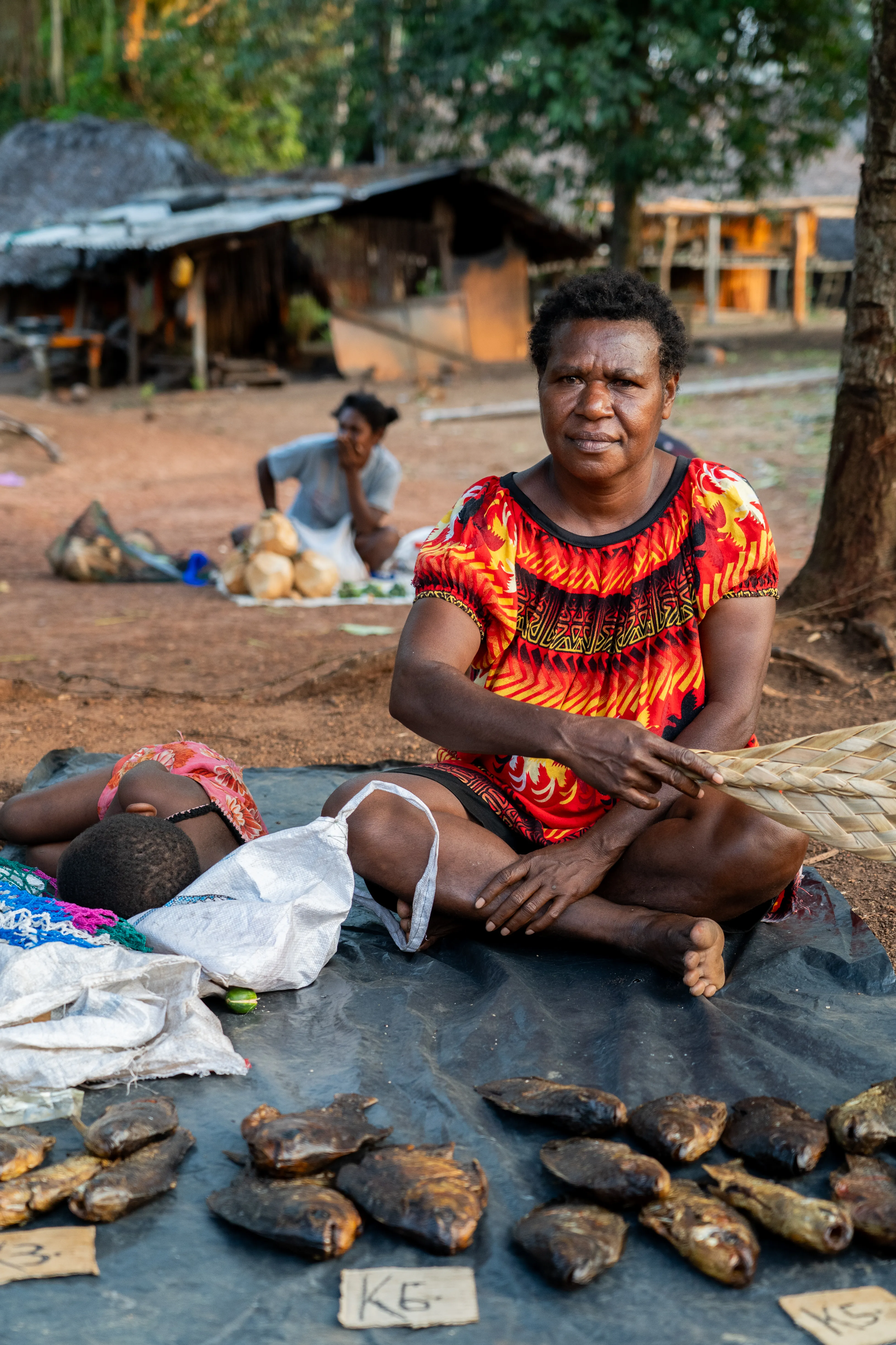 Woman selling smoked fish at market with her baby there, Papua New Guinea