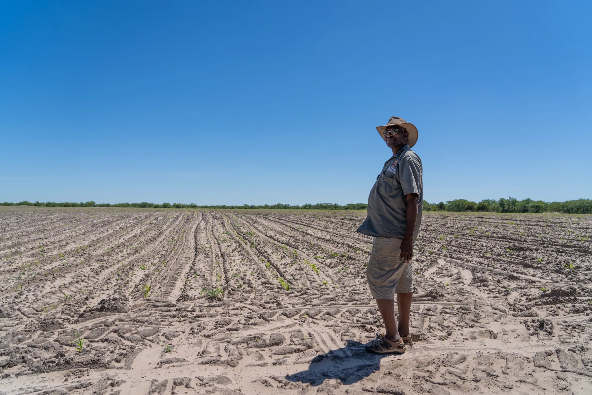 Farmer stands amid freshly plowed fields under open sky, Botswana