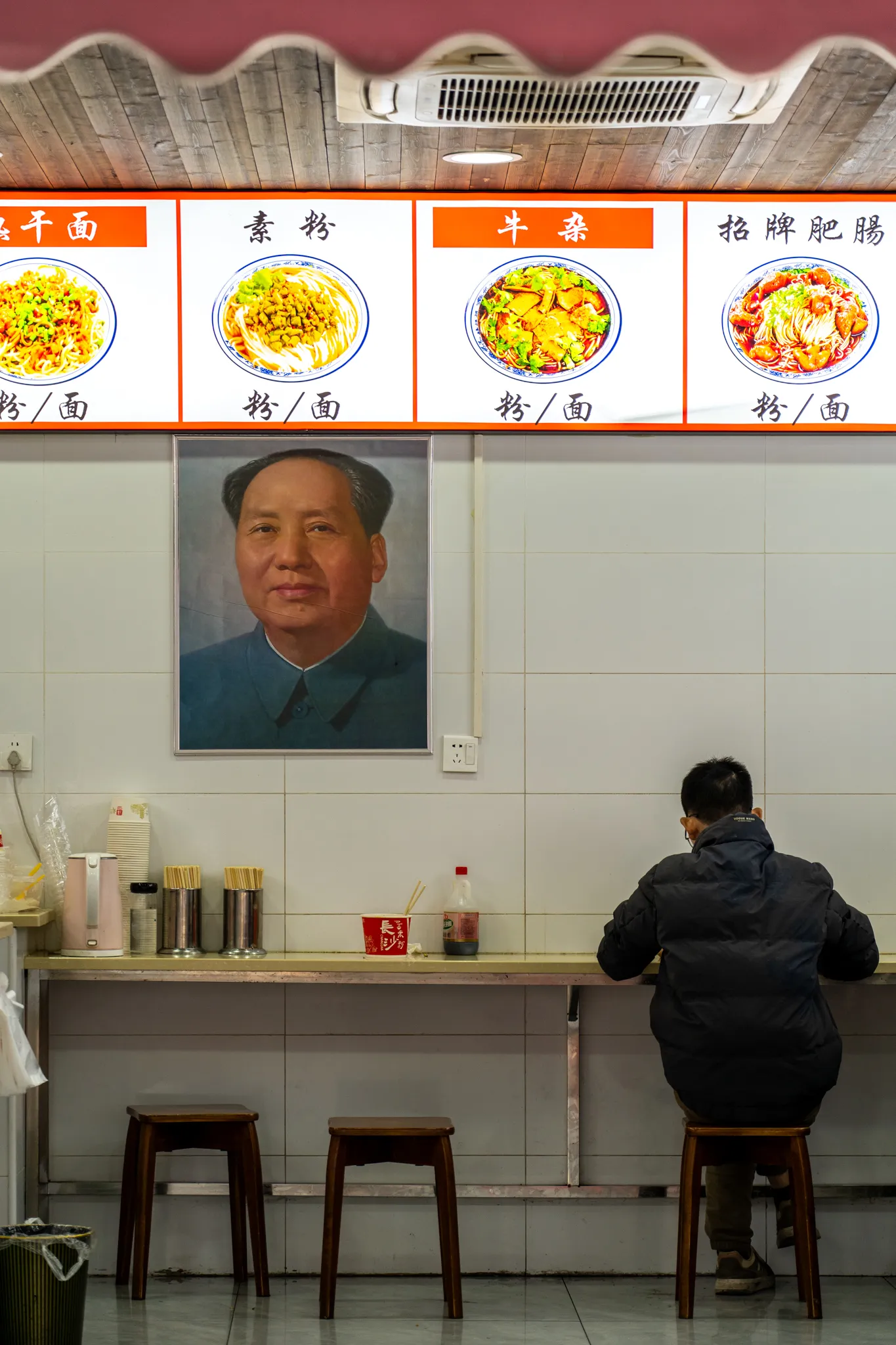Noodle shop diner beneath a Mao portrait in Wuhan, China