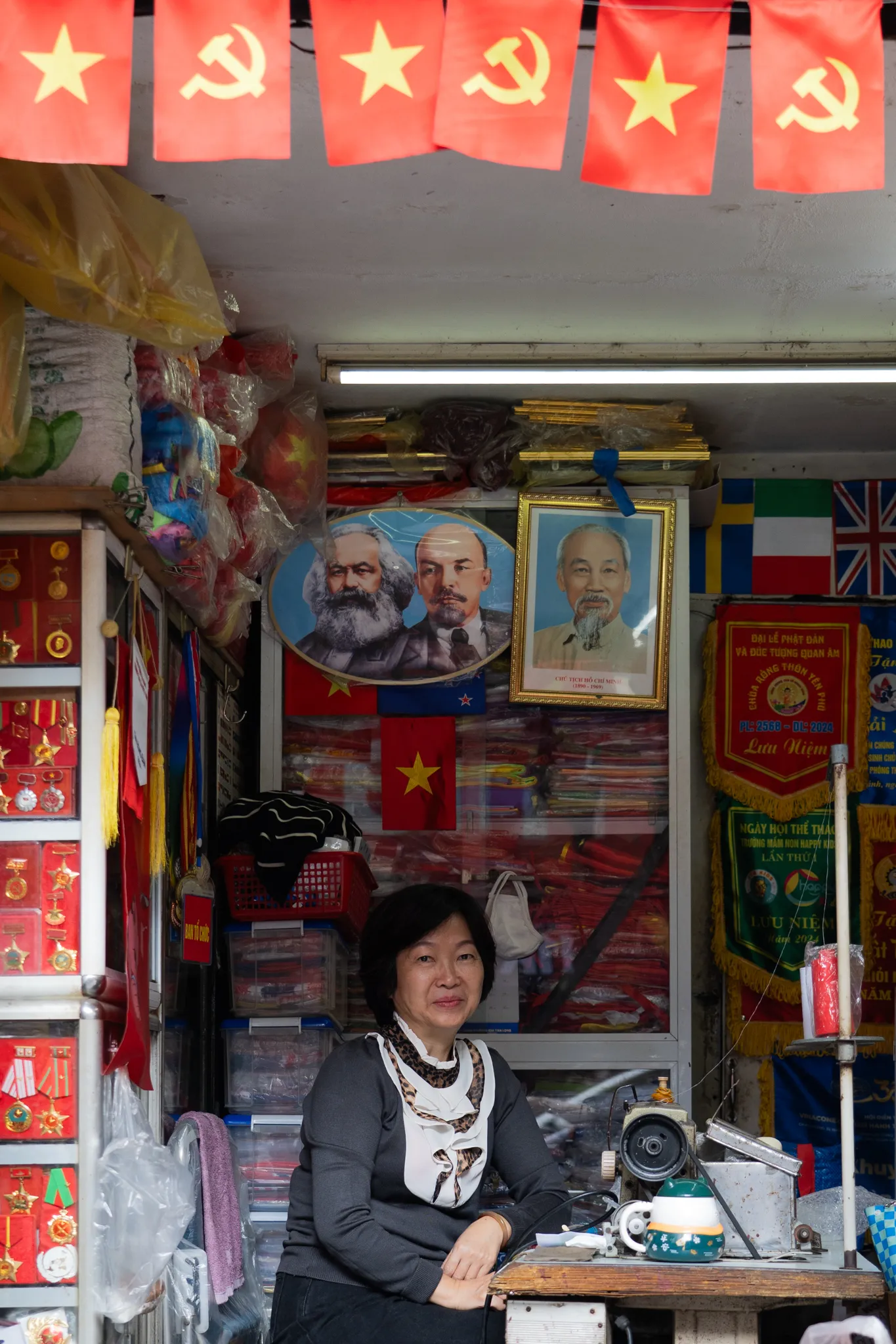 Shopkeeper beneath a portrait of Ho Chi Minh in Hanoi, Vietnam